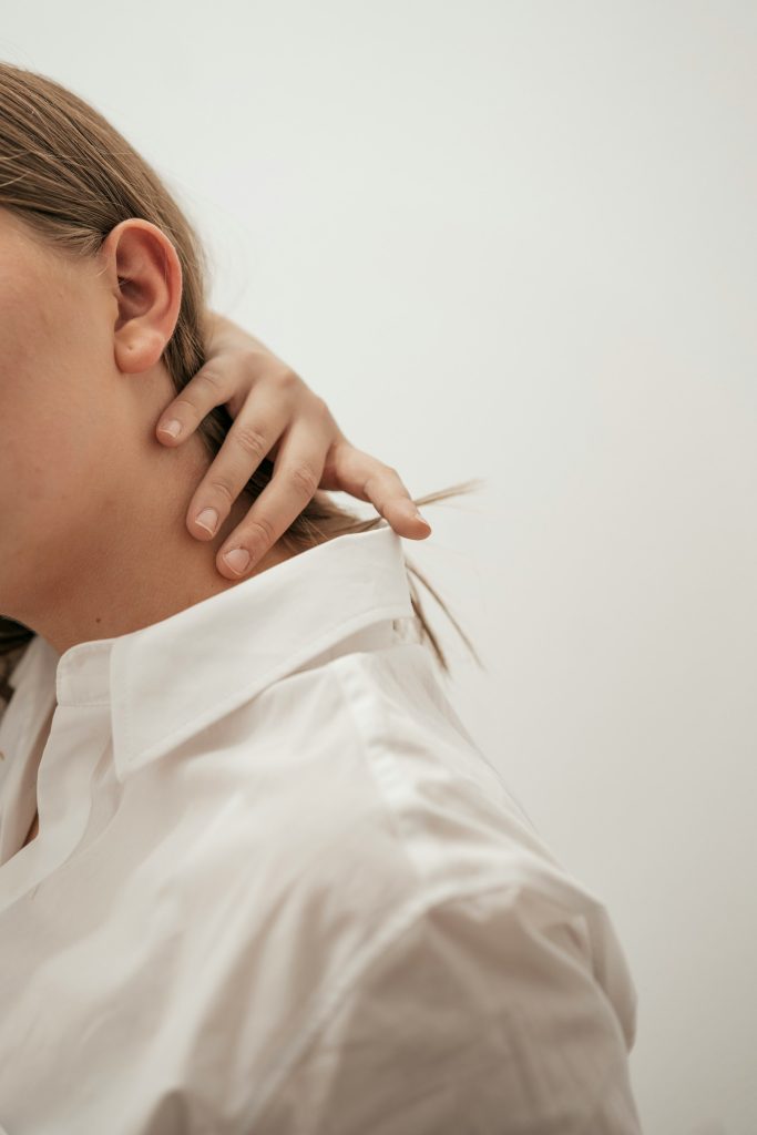 Person holding the side of their neck and shoulder, clothed, showing tension
