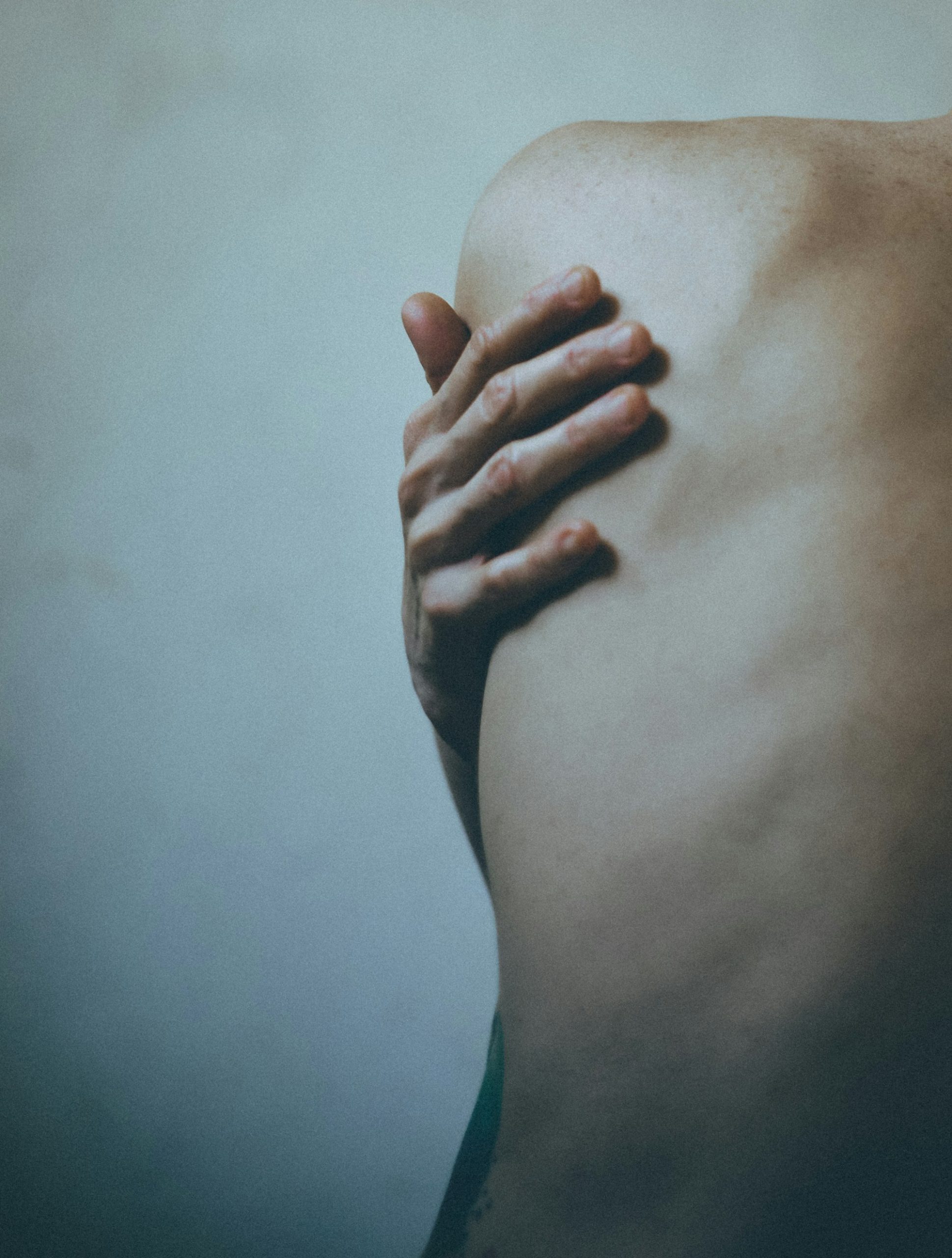 Person reaching to hold the back of their shoulder, guarding a painful joint