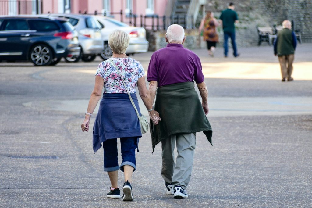 Older couple walking outdoors, seen from behind, holding hands