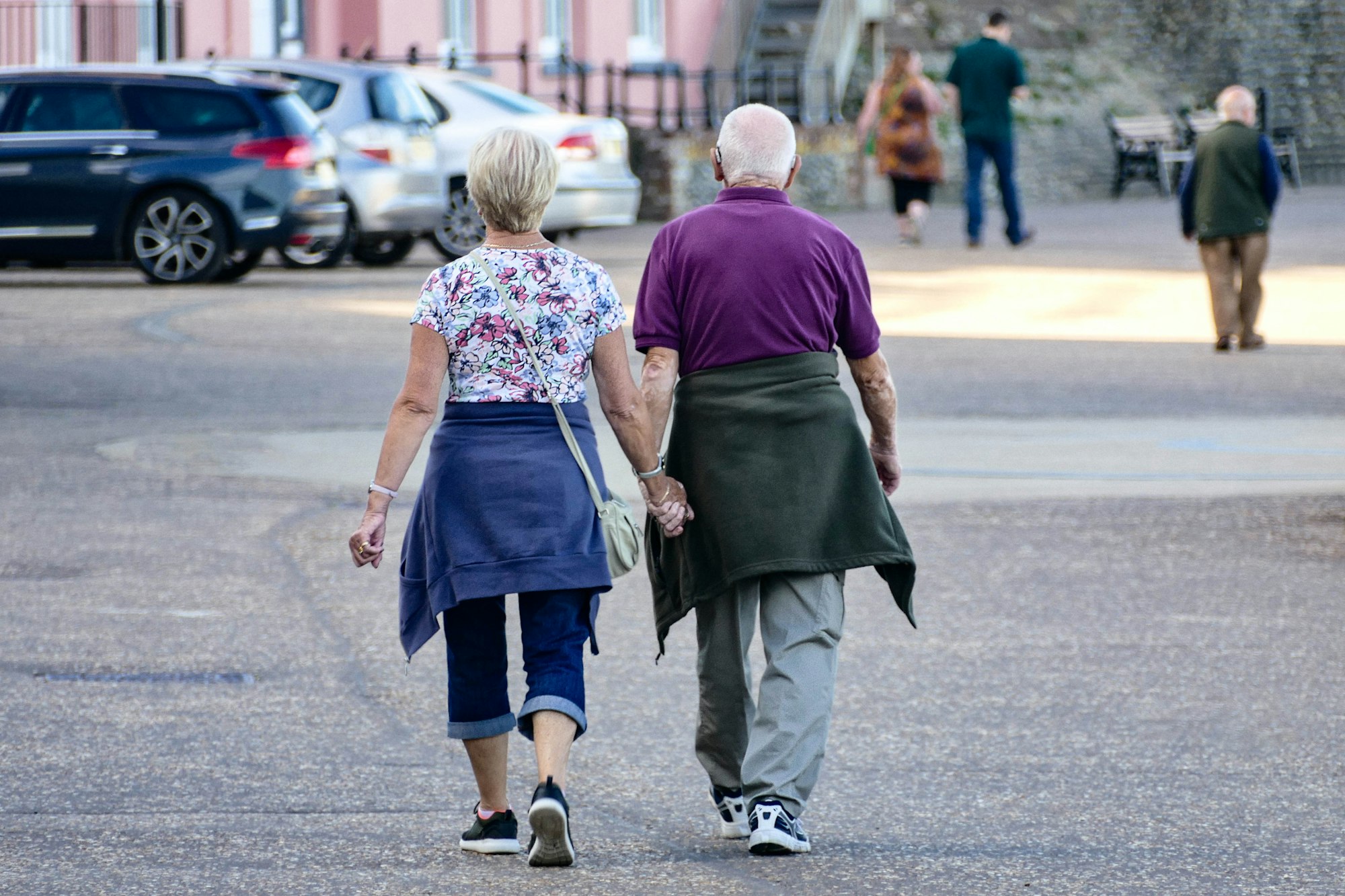 Older couple walking outdoors, seen from behind, holding hands